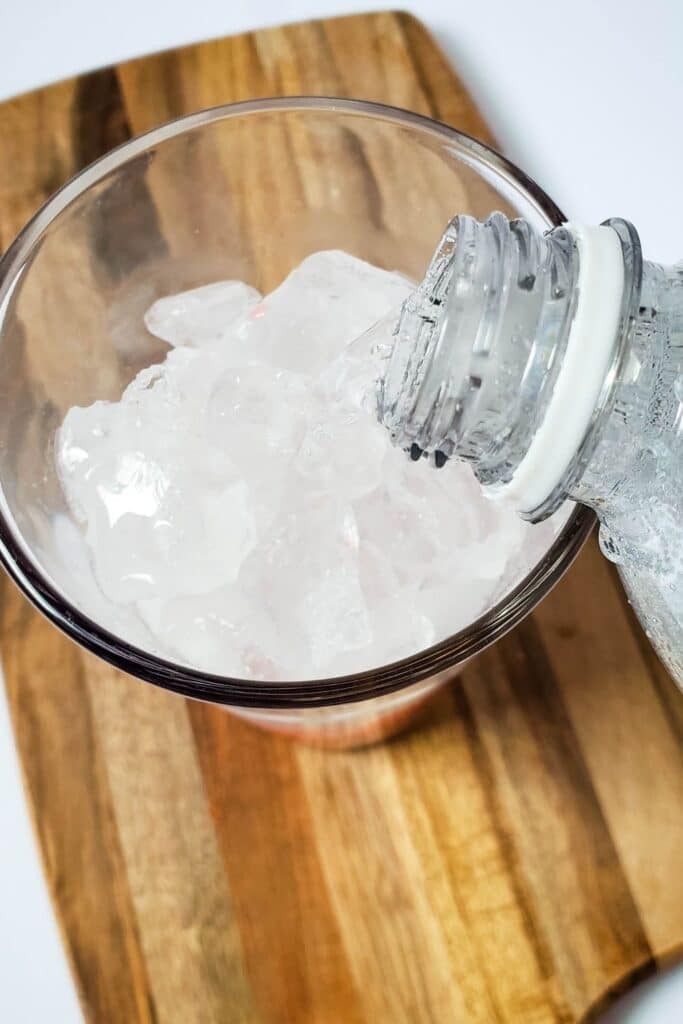 pouring club soda into glass with ice 