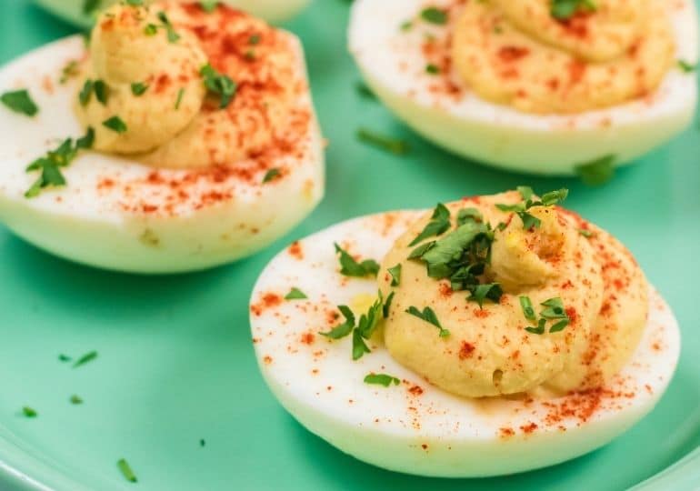 deviled eggs on a green plate, topped with garnish