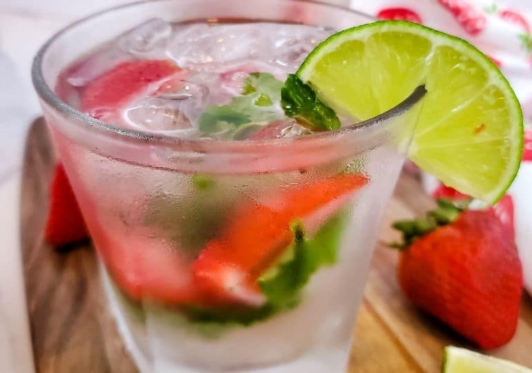 strawberry mojito in a glass garnished with a lime wedge on table