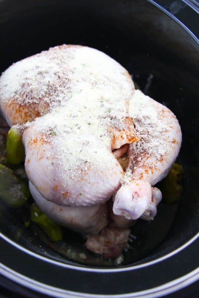 whole chicken in crockpot with seasoning sprinkled all over the top