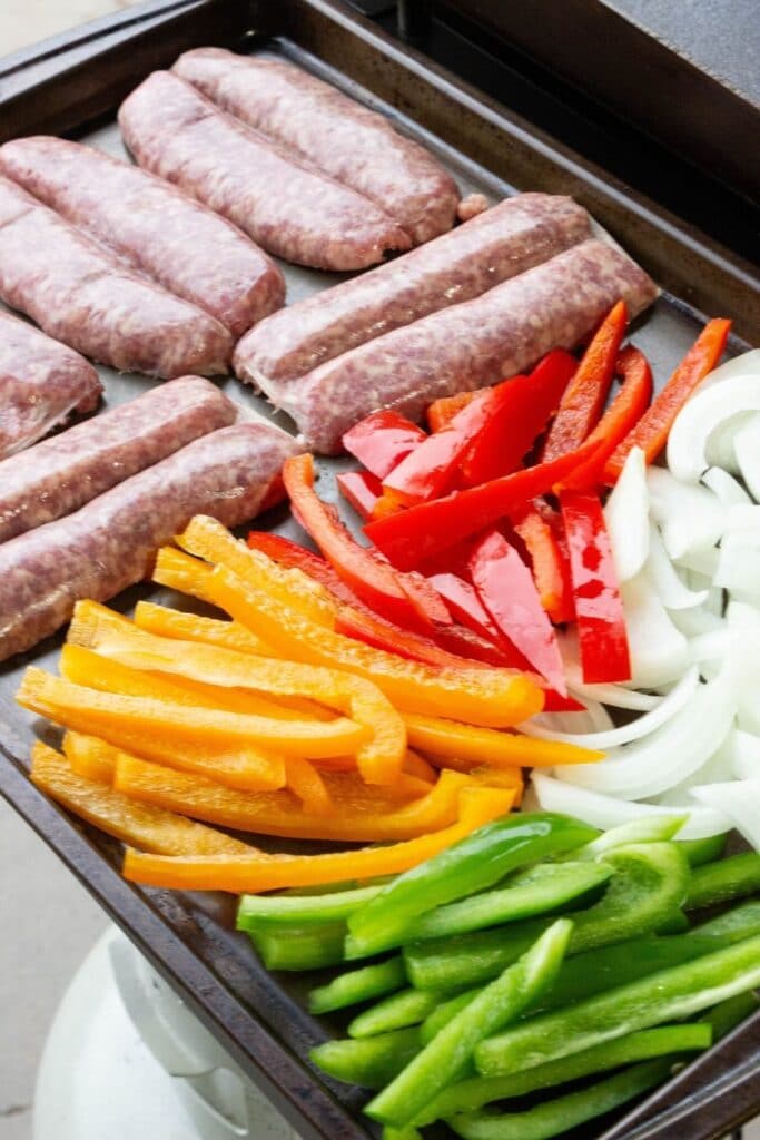 brats and peppers and onions on a baking sheet