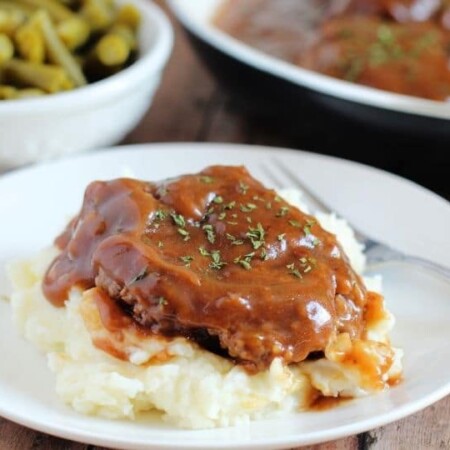 salisbury steak on a plate with pan and veggie behind it