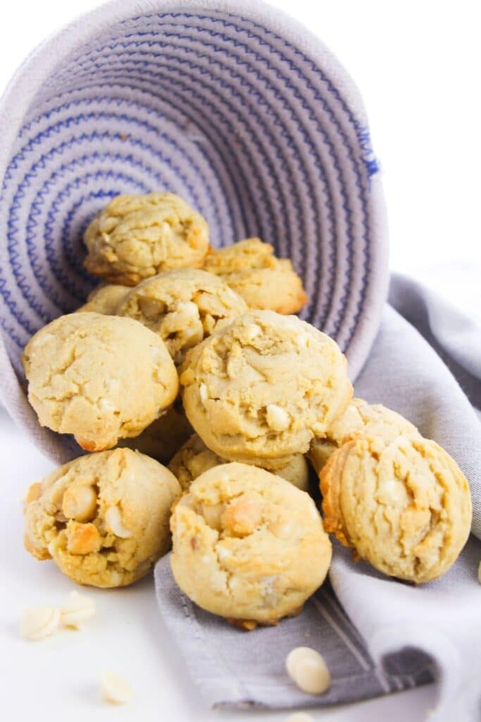 macadamia cookies poured out of a woven basket on table 