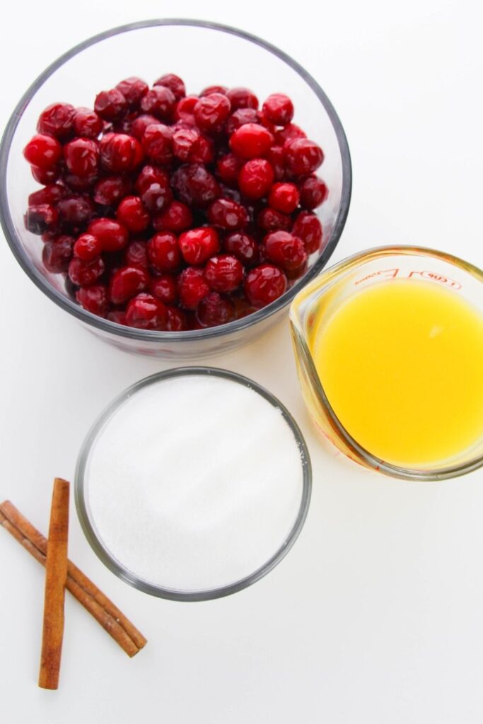 cranberries, juice, sugar and cinnamon sticks on white counter 