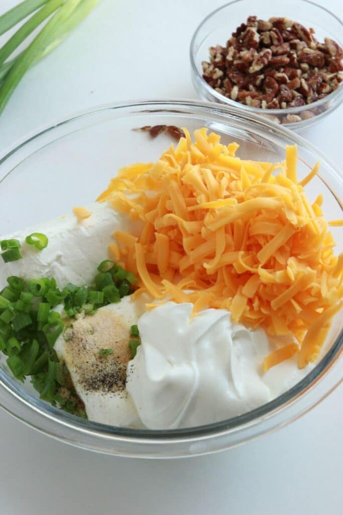 cheese, cream cheese, green onions, and spices in a bowl with pecans in a bowl behind on counter