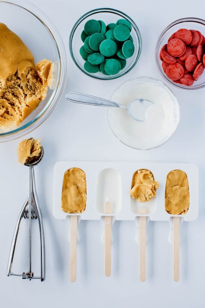 cake popsicles in the making with candy melts in bowls, and cake batter in a bowl