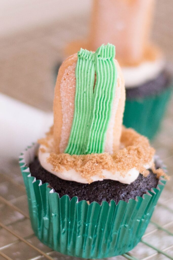 piiping green frosting around lady finger cookie in center of cupcake