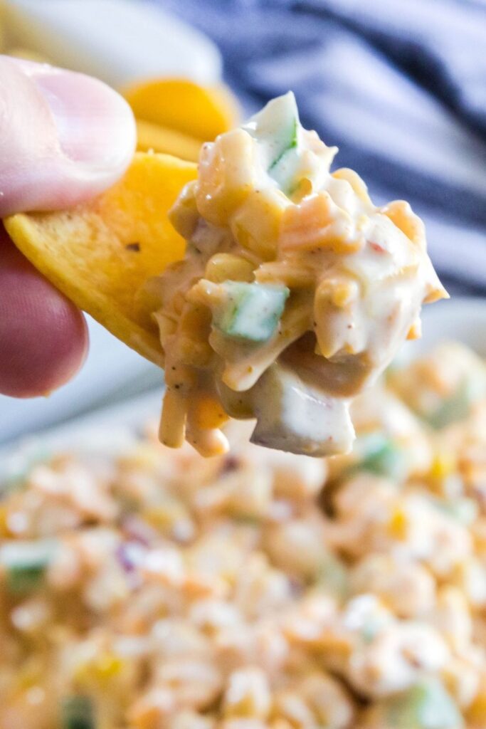 Frito scoop with corn dip in it being held above bowl