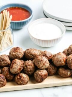 meatballs on a platter with sauce in containers behind it