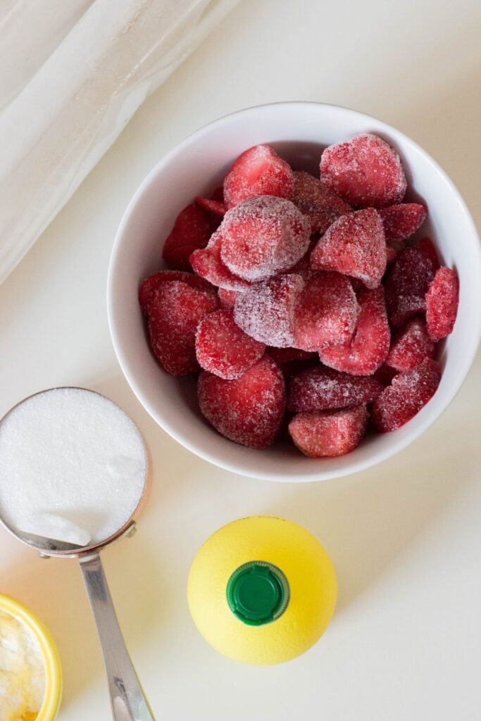 overhead shot of strawberries in bowl, puff pastry, sugar, and lemon juice on counter 