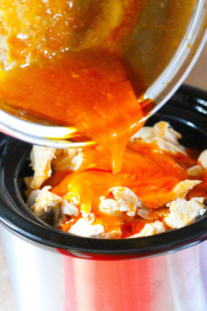 buffalo chicken dip in crockpot and pouring sauce over the top