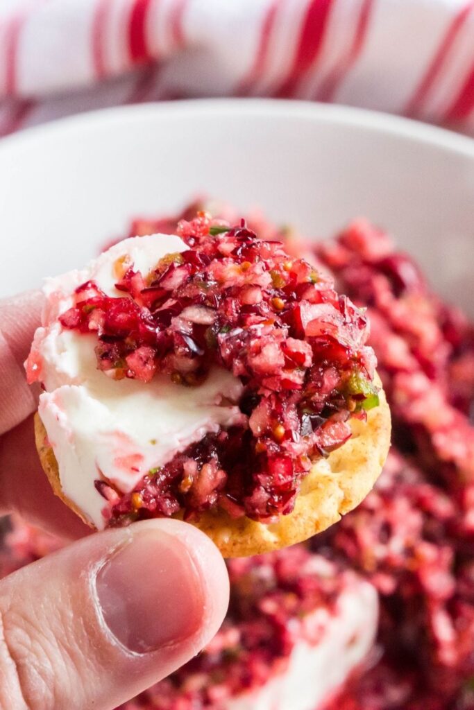 holding cracker with cram cheese and jalapeno salsa