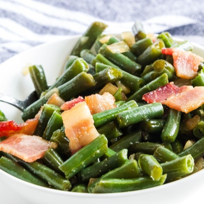 bowl of green beans with bacon on top 