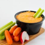 creamy chicken dip with celery stick in bowl on white counter