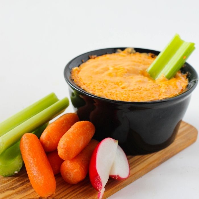 creamy chicken dip with celery stick in bowl on white counter 