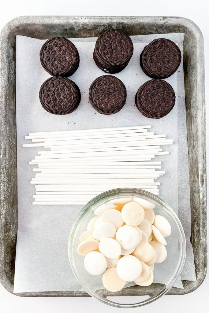 Oreos, cake pop sticks and white chocolate on a cookie sheet 