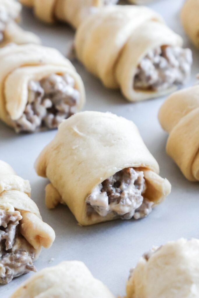 crescent rolls wrapped in sausage on a baking sheet 