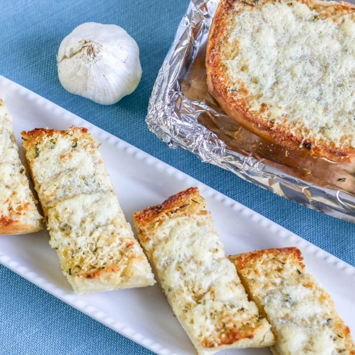 garlic bread on tray with pan of garlic bread behind it