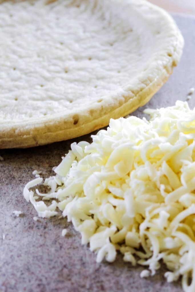 pizza crust and shredded cheese on table 