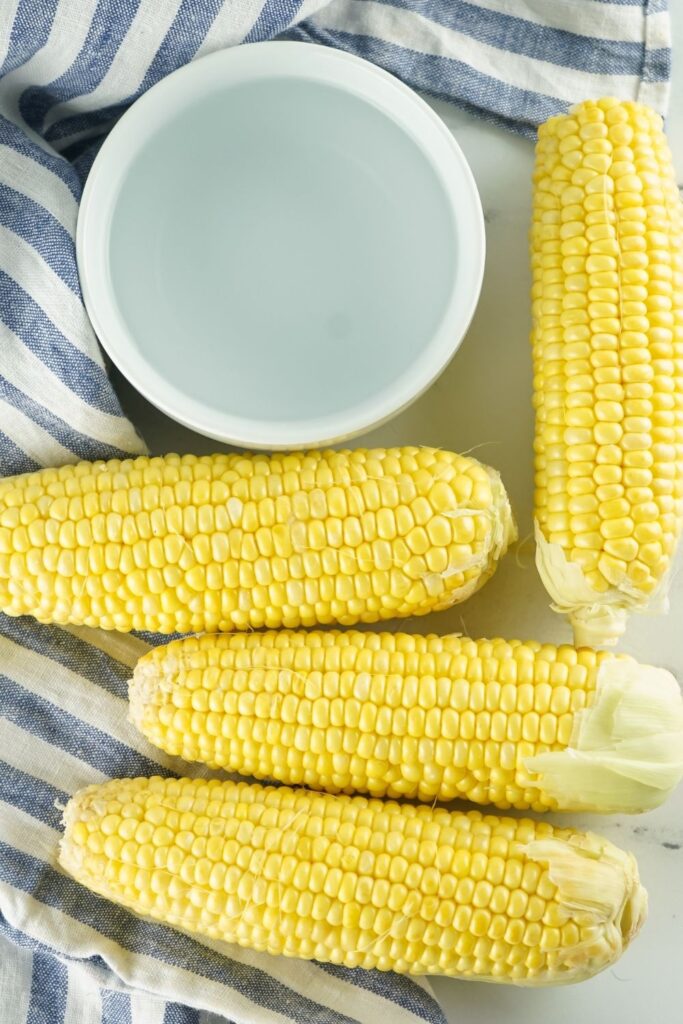 corn on the cob and bowl of water with towel by it 