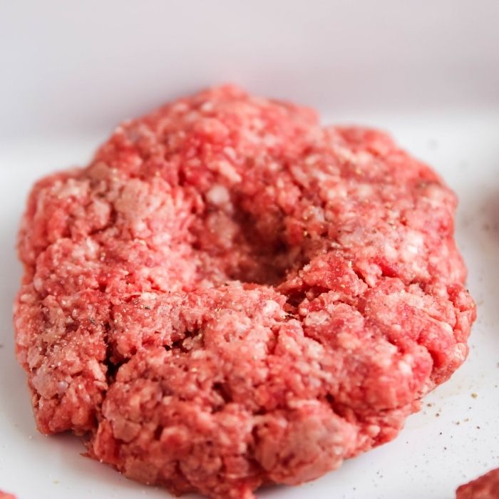 Closeup of hand salting beef burgers cooking on electric grill at