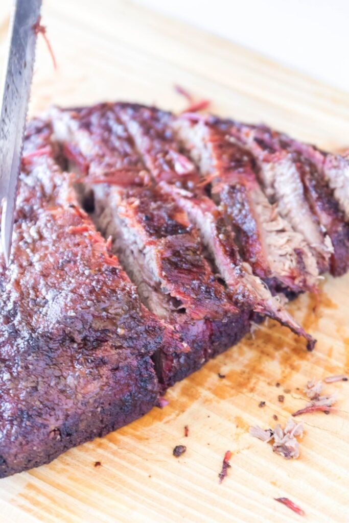 tender brisket being sliced on cutting board 