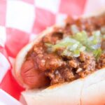 close up of chili dog in basket topped with chili and relish