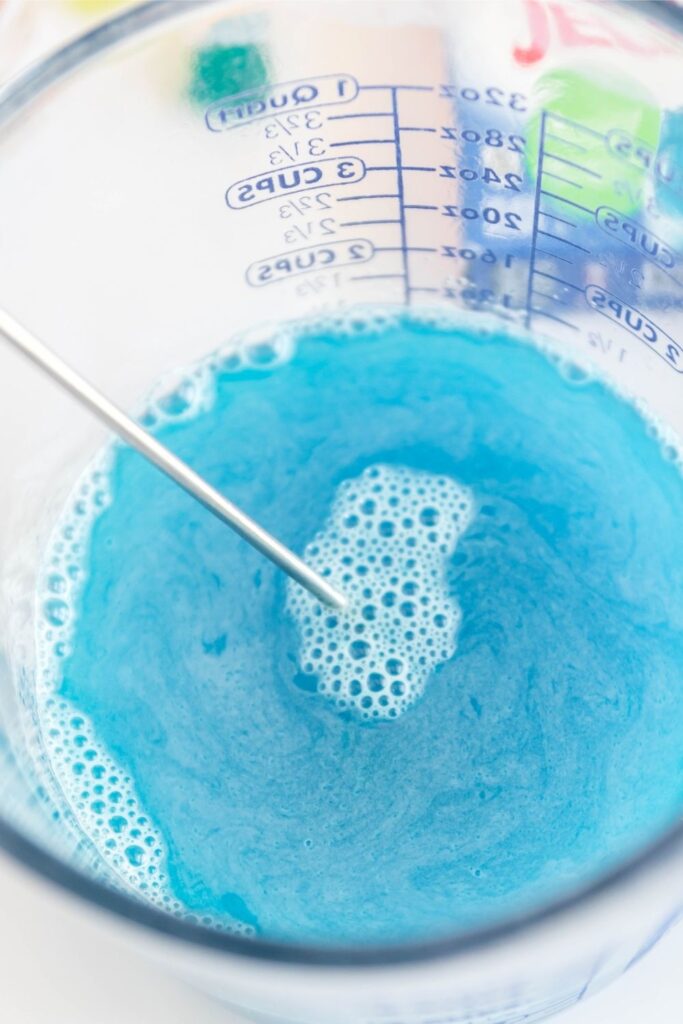 blue jello in a measuring cup with whisk in bowl 