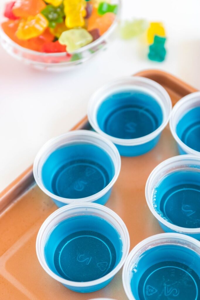 vodka jello shots on a tray with gummy bears in a bowl behind it 