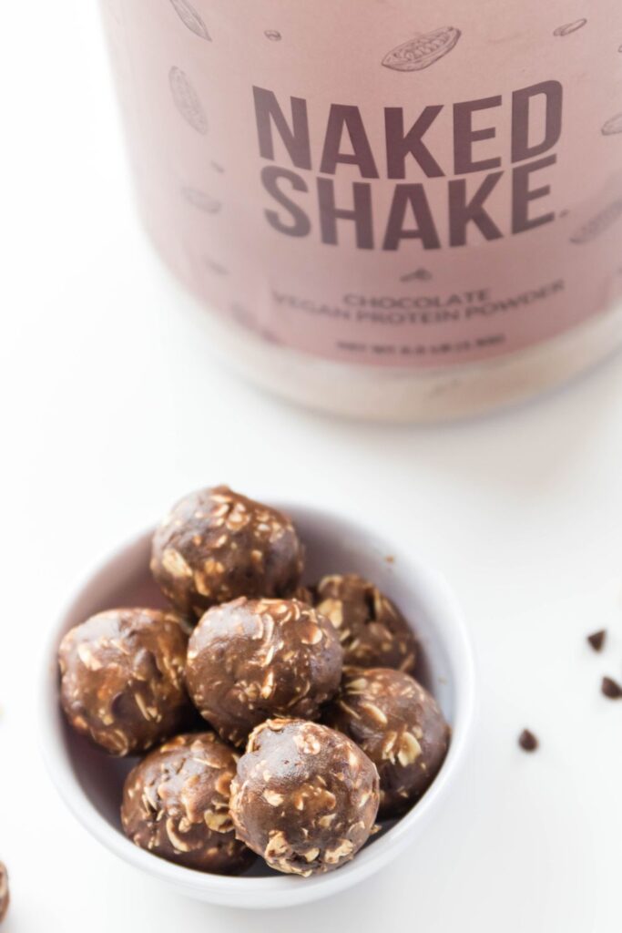 peanut butter chocolate protein balls in a bowl with jug of protein powder behind it