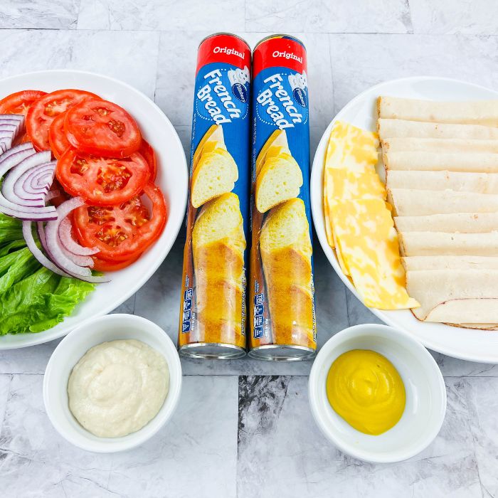 lunch meat, cheese, and toppings on plates on a marble counter 