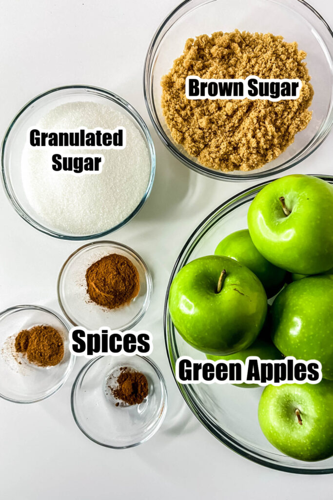 apples, sugar and spices in glass bowls on white counter 