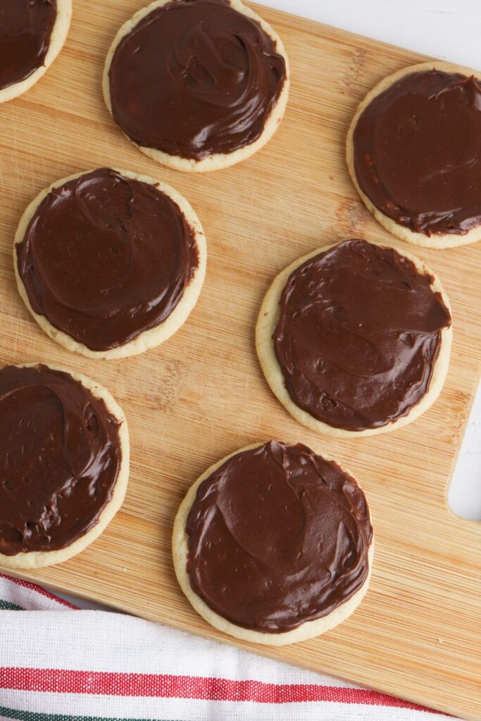 sugar cookies frosted with chocolate frosting on wooden cutting board