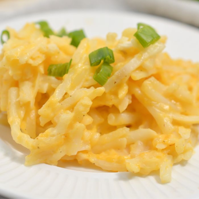 cheesy hashbrowns on a white plate topped with diced green onions 