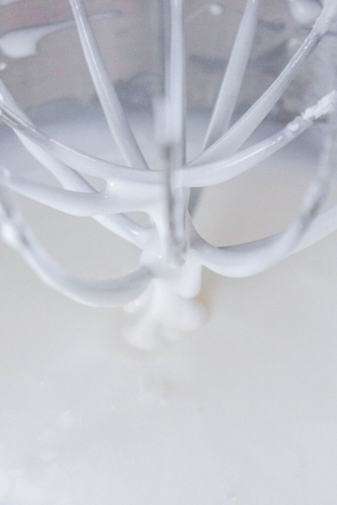 close up of whisk attachment in stand mixer with royal icing on it 