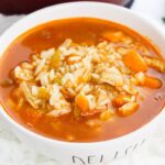 cajun chicken and rice soup in a white bowl with word delish on front