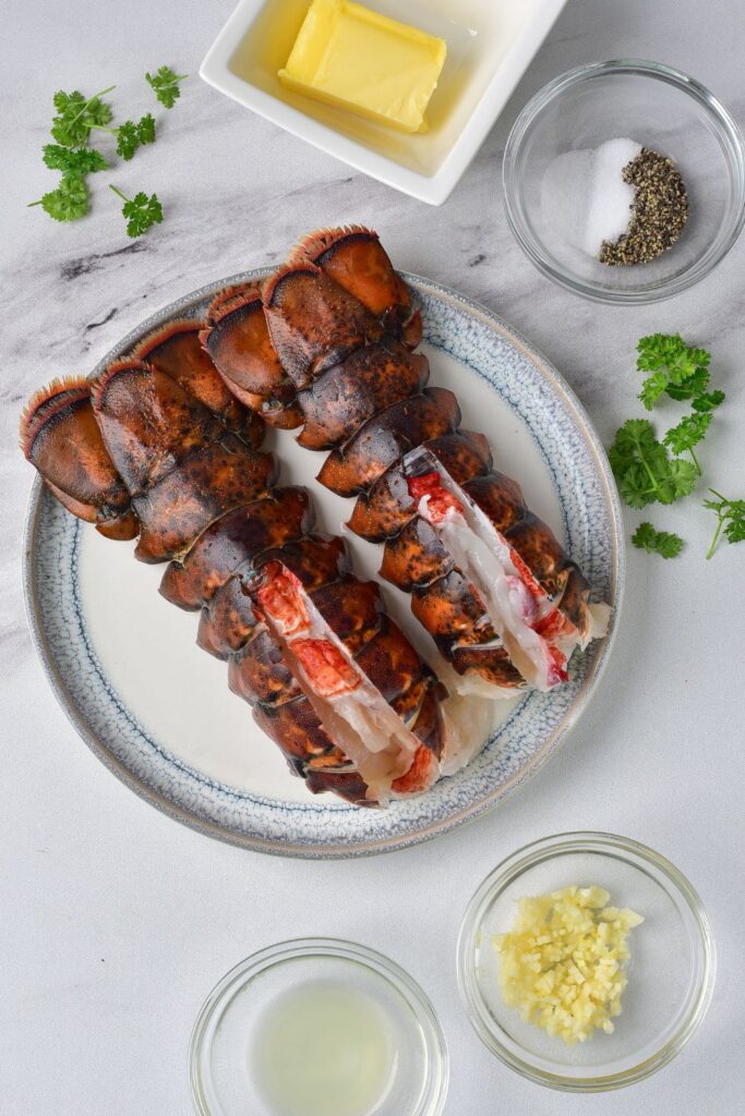 raw lobster on a plate with butter, spices, and fresh herbs on marble countertop