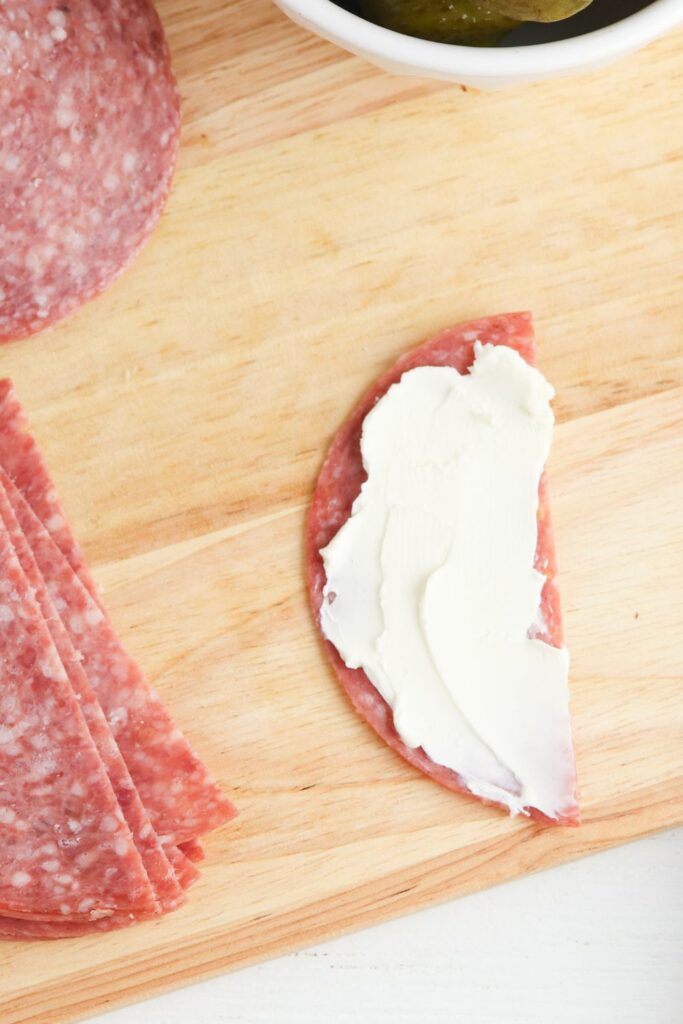 salami with cream cheese spread on top, on cutting board