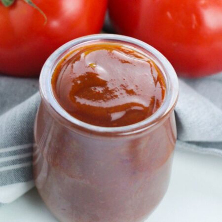 enchilada sauce in a little jar on table with tomatoes behind it