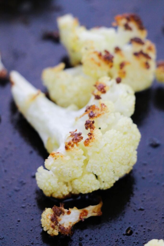 parmesan cauliflower on a dark baking sheet 