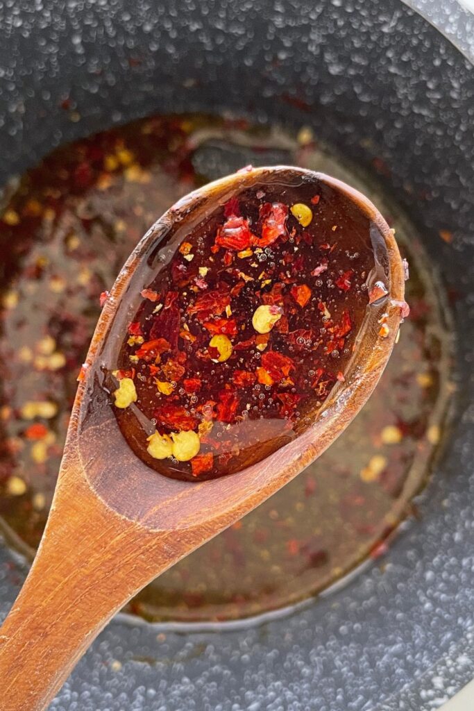 wooden spoon with some hot honey and red pepper flakes in spoon above saucepan