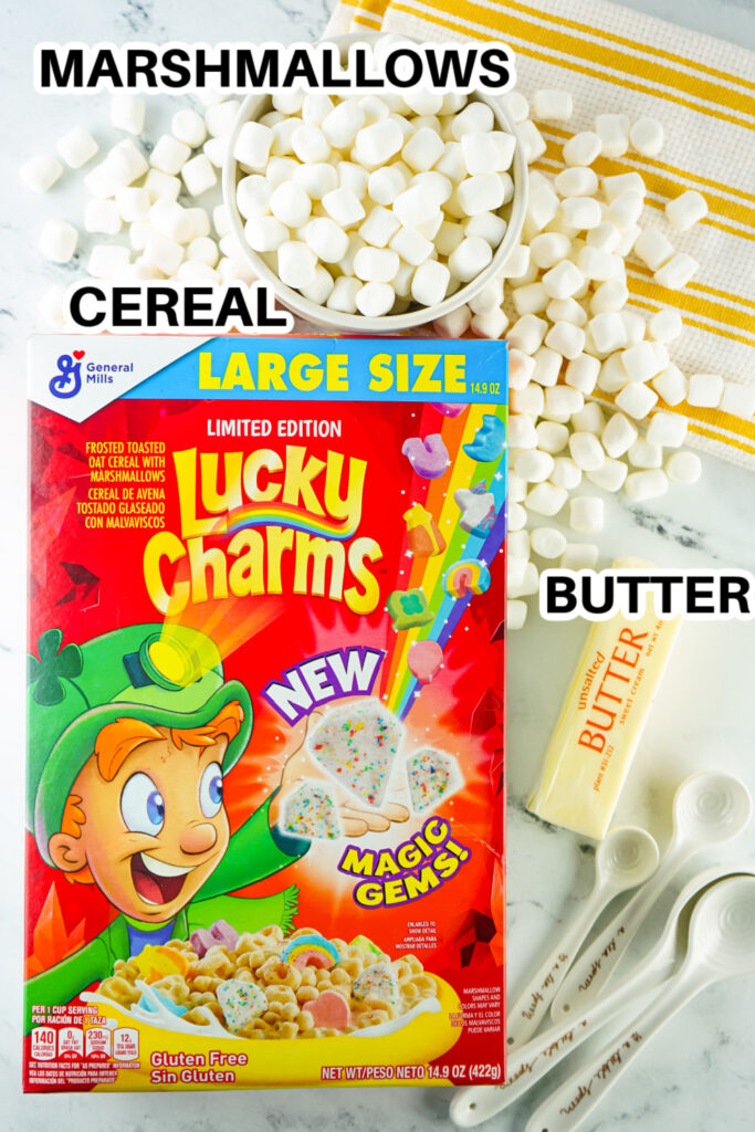 ingredients for lucky charm bars on a white counter with spoons and towel on side of picture 