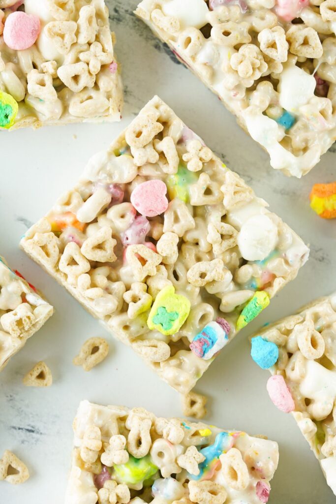 lucky charm bars sliced into squares on white marble counter with extra cereal spread around bars 