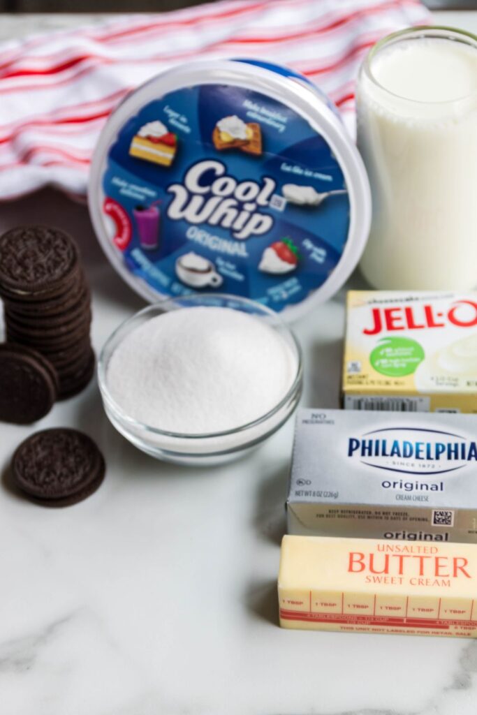 Oreo dessert ingredients on counter, milk, jello, butter, cream cheese, Oreo cookies and tub of cool whip 