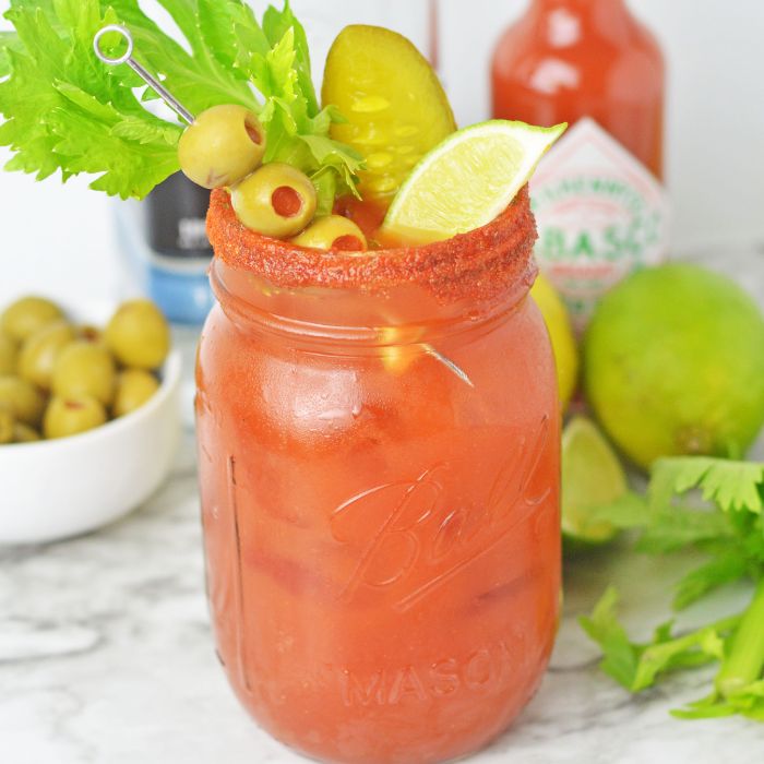 a bloody maria in a glass on a counter with garnishes behind it 