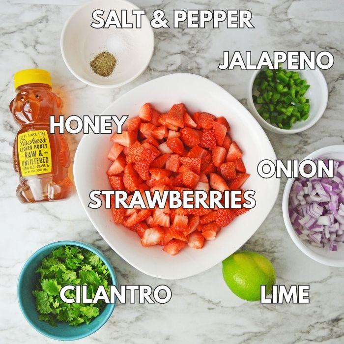 ingrdients for strawberry salsa in bowls on counter. Diced strawberries, jalapneo, salt and pepper, honey, onion, lime and cilantro