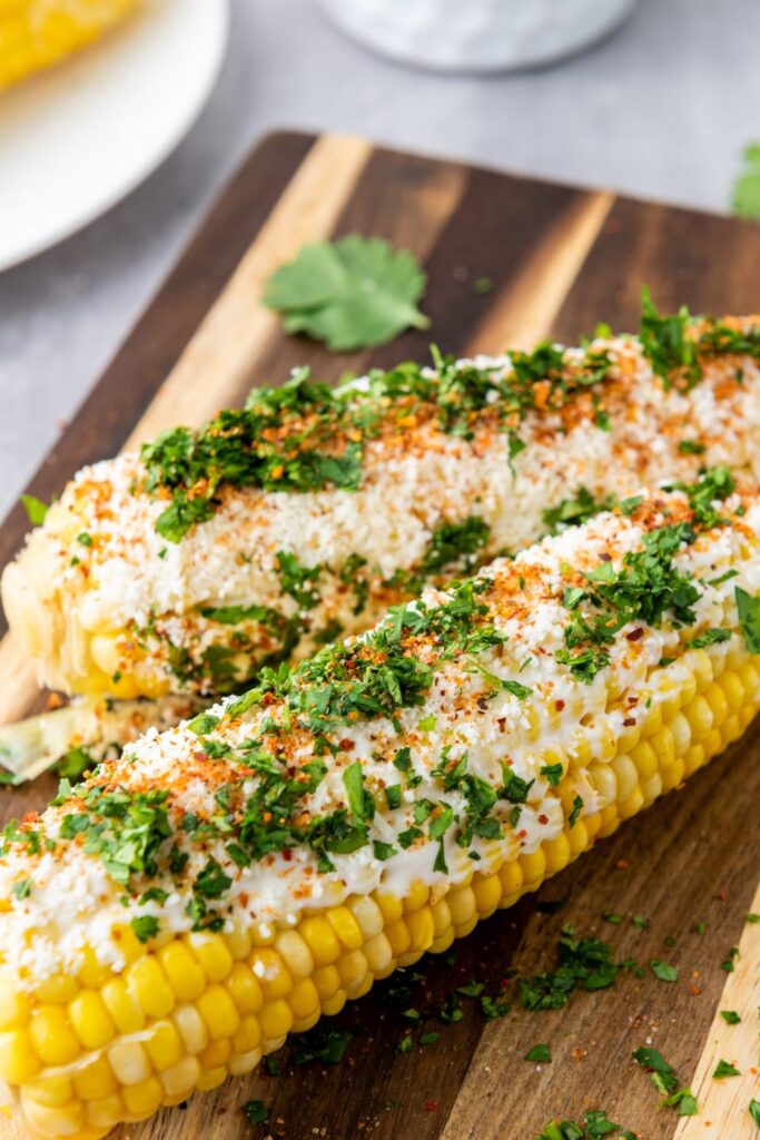 street corn on the wooden cutting board topped with garnish 