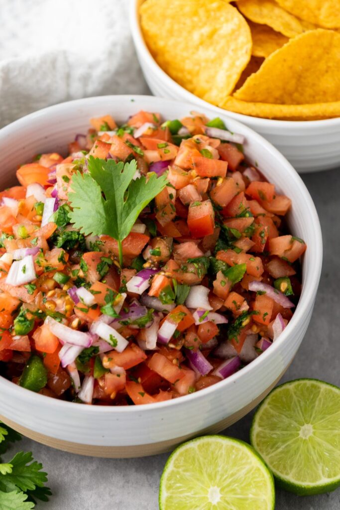 bowl with chunky salsa, sliced lime in front and bowl of chips sitting behind salsa 