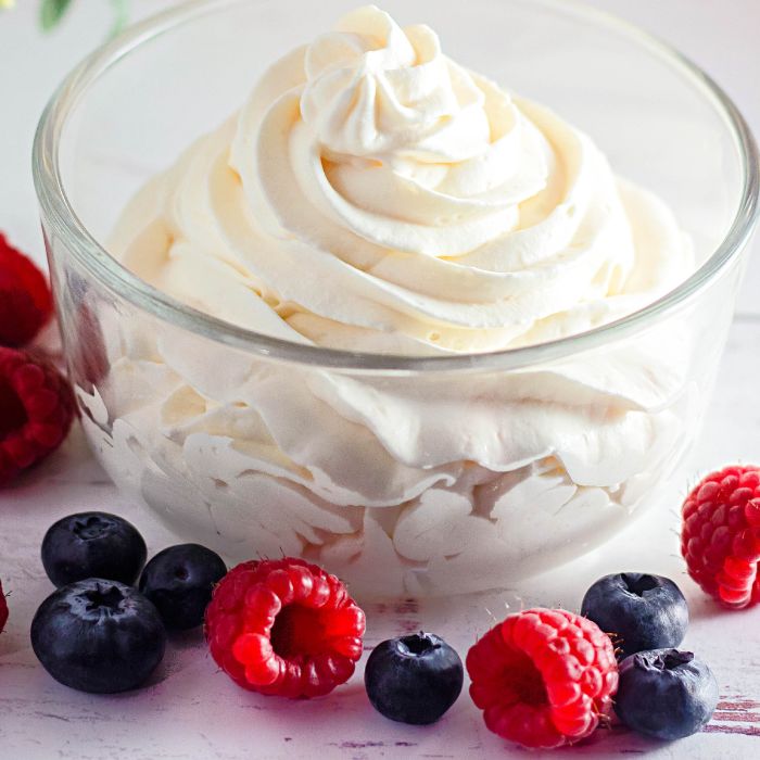 stabilized whipped cream in a glass jar on counter with fresh berries around the bowl 