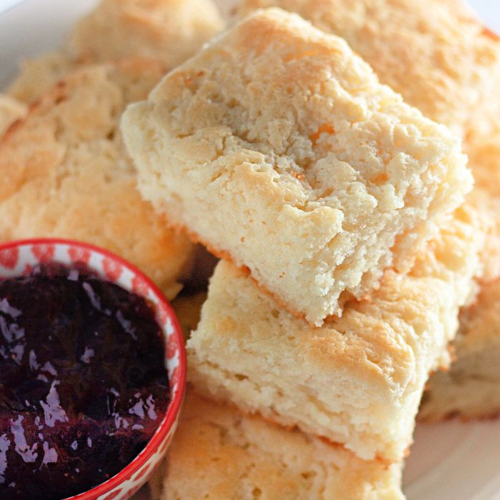 7 Up Biscuits stacked on a plate with a bowl of grape jelly on side